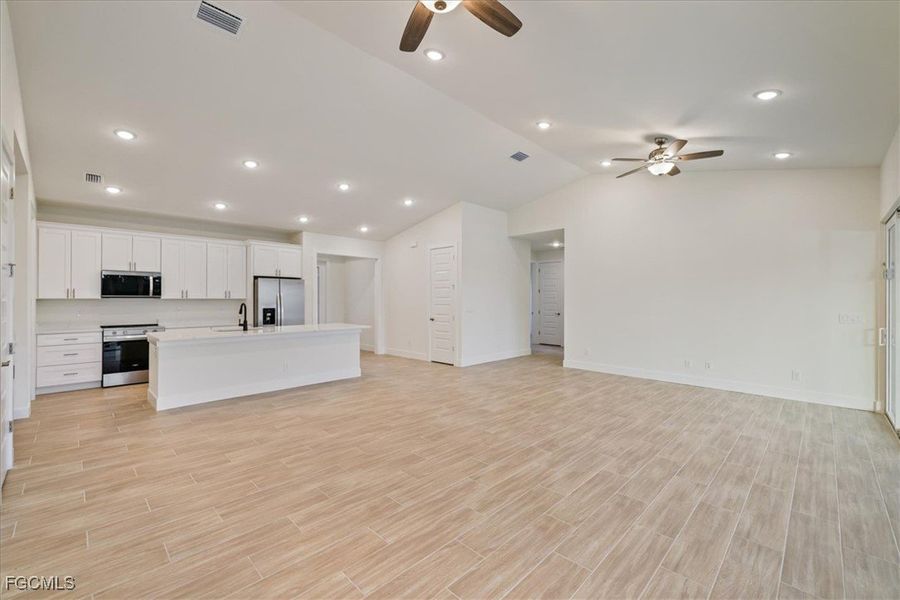Kitchen with open floor plan, recessed lighting, white cabinets, a kitchen island with sink, and stainless steel appliances