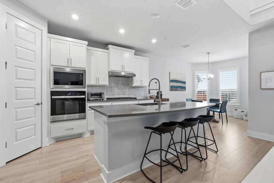 Kitchen featuring stainless steel appliances, white cabinetry, decorative backsplash, and a breakfast bar area
