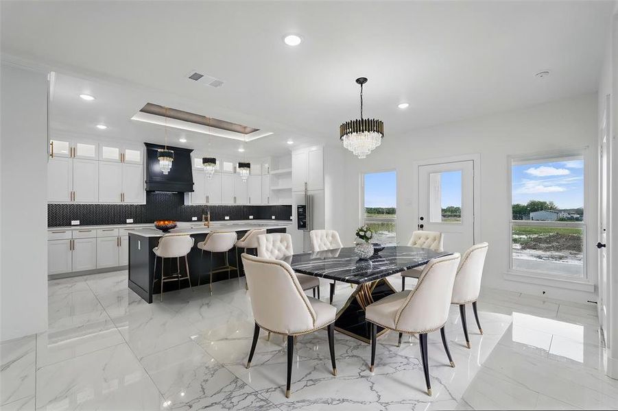 Dining area featuring light marble finish flooring, a chandelier, recessed lighting, and a tray ceiling Dining area featuring light marble finish flooring, a chandelier, recessed lighting, and a tray ceiling