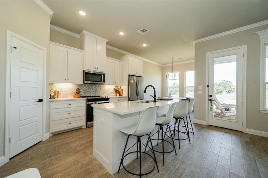 Kitchen with a center island with sink, appliances with stainless steel finishes, a kitchen bar, backsplash, and white cabinetry Kitchen with a center island with sink, appliances with stainless steel finishes, a kitchen bar, backsplash, and white cabinetry