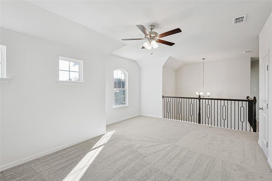 Empty room with ceiling fan with notable chandelier, light carpet, and vaulted ceiling