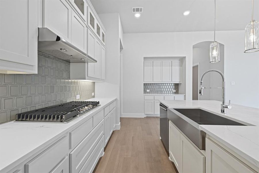 Kitchen featuring white cabinets, tasteful backsplash, pendant lighting, light wood-style floors, and light stone countertops Kitchen featuring white cabinets, tasteful backsplash, pendant lighting, light wood-style floors, and light stone countertops