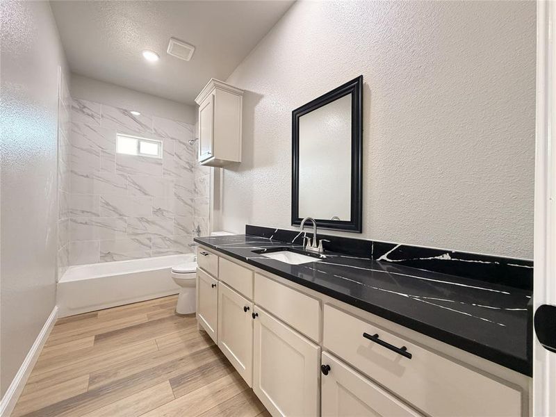 Bathroom with vanity, a textured wall, light wood-type flooring, and shower / bathtub combination