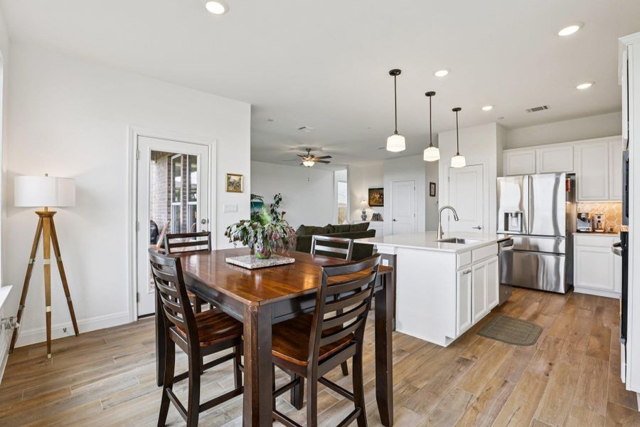This spacious kitchen features white cabinetry, a large kitchen island with a sink, and stainless steel appliances, including a refrigerator