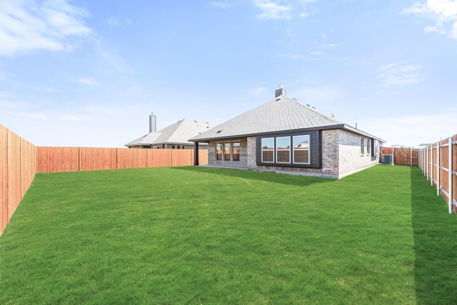 Brick home rear exterior with large grassy backyard enclosed by wood privacy fence Brick home rear exterior with large grassy backyard enclosed by wood privacy fence