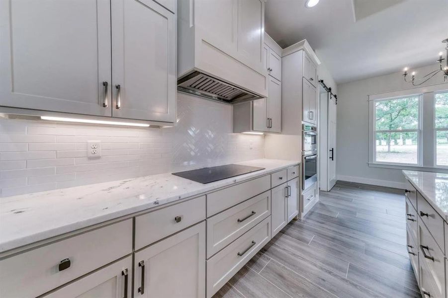 Kitchen featuring black electric stovetop, white cabinets, a barn door, custom exhaust hood, and light hardwood / wood-style flooring