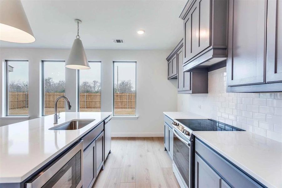 Kitchen featuring stainless steel appliances, a sink, baseboards, light wood finished floors, and decorative backsplash
