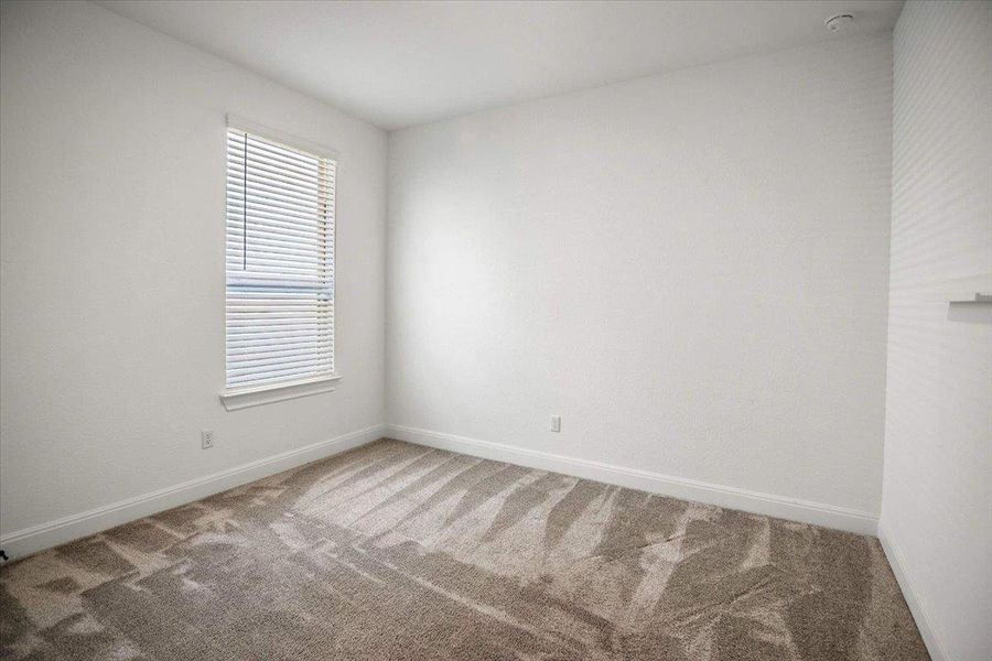 A well-lit bedroom features plush carpeting and a window with blinds, offering comfort and privacy.