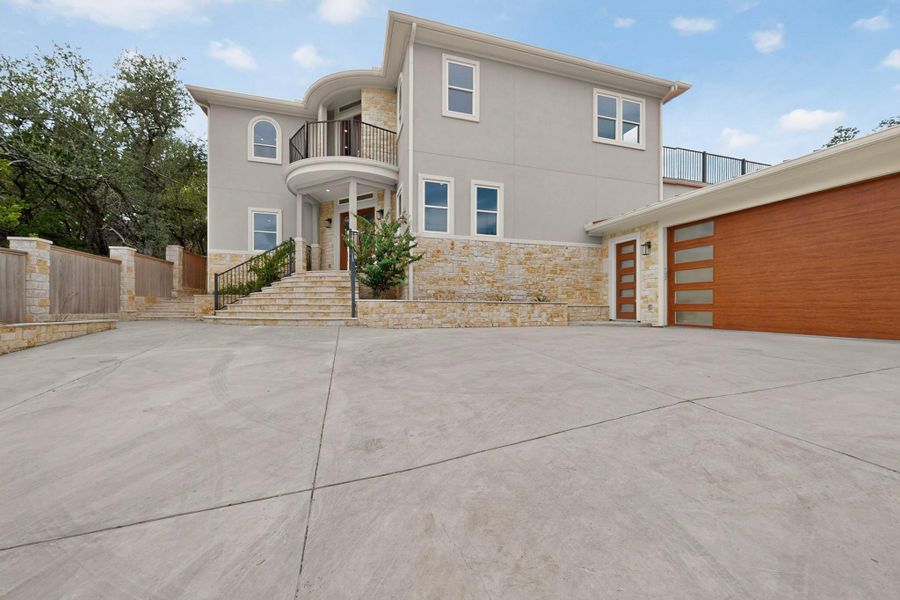 A spacious concrete driveway leads to this modern home featuring stone accents and wood-look garage doors.