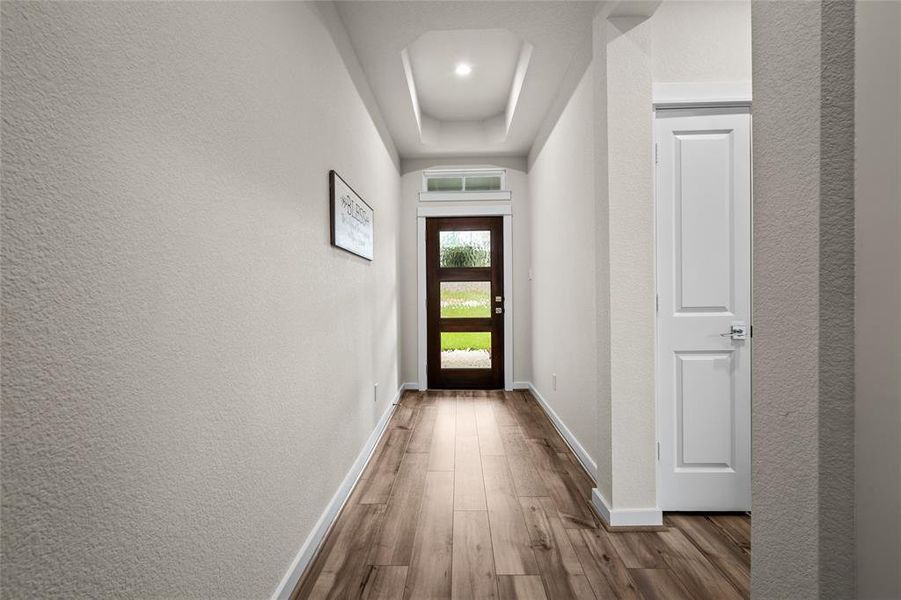 This well-lit hallway featuring a look toward the front wood and glass front door that allows natural light to enter the home. The neutral wall colors, trayed ceiling lighting, and front door with glass panels that allows natural light to enter.