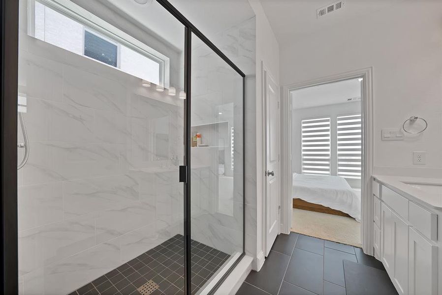 Spacious walk-in shower with black-framed glass enclosure, white marble-look tile surround, and dark tile flooring