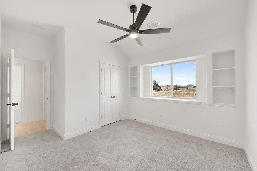 Empty bedroom with vaulted ceiling, ceiling fan, built-in shelves, closet, and carpet flooring