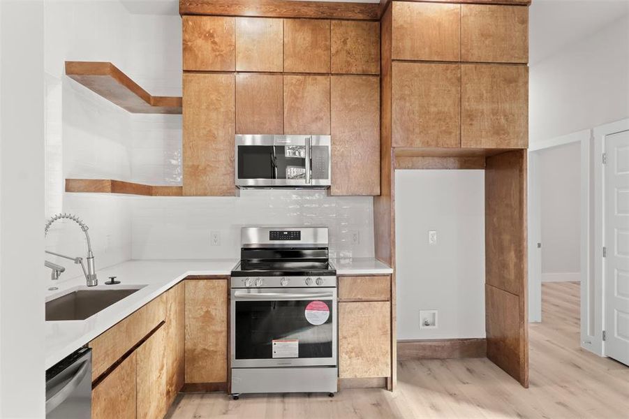 Kitchen featuring decorative backsplash, sink, light wood-type flooring, and stainless steel appliances