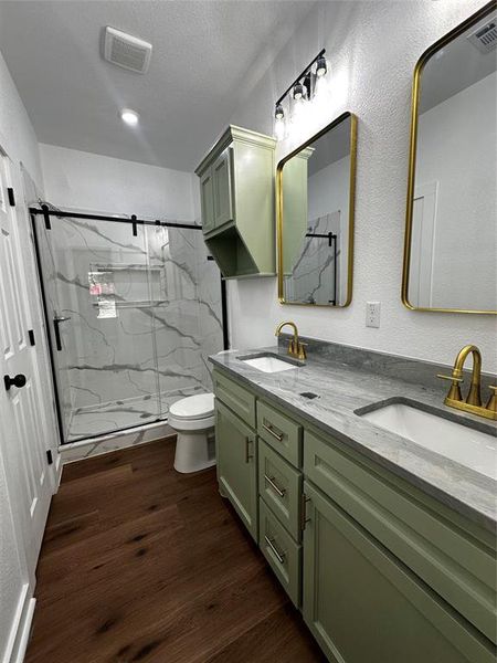 Bathroom featuring a dual vanity with light green cabinetry, gray stone countertops, and gold-finish fixtures