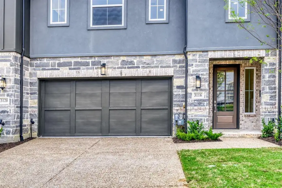 Contemporary facade featuring a stone and stucco exterior, a paneled garage door, a glass-paneled entry door, a concrete driveway, and exterior light fixtures