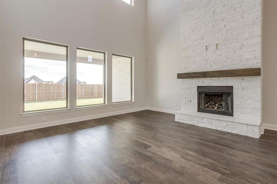 Unfurnished living room with a towering ceiling, a stone fireplace, and dark hardwood / wood-style floors