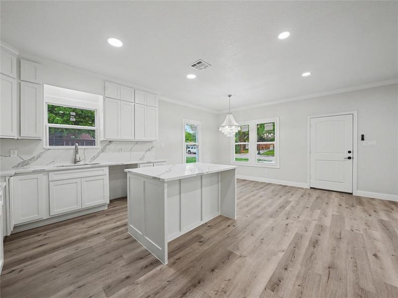 Bright kitchen featuring white shaker cabinetry, white countertops with veining, a central island, recessed lighting, and wood-finish flooring