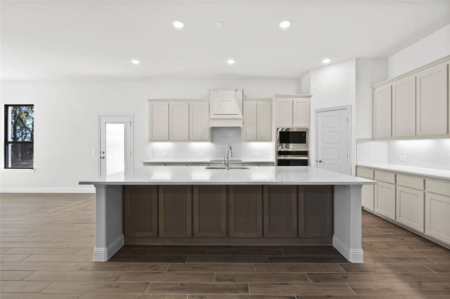 Kitchen with dark wood-type flooring, custom range hood, recessed lighting, light stone counters, and backsplash Kitchen with dark wood-type flooring, custom range hood, recessed lighting, light stone counters, and backsplash