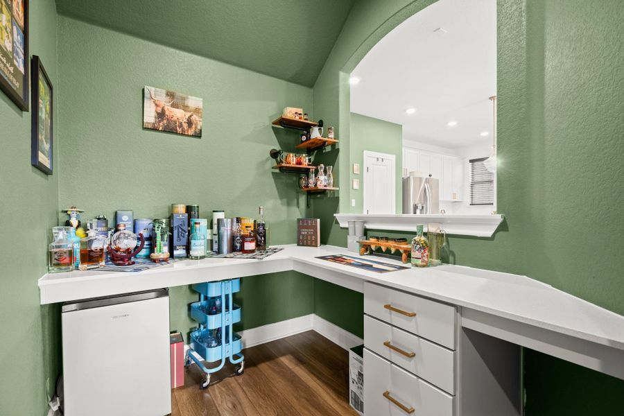 Bar with white fridge, white cabinetry, a textured wall, dark wood-style floors, and light countertops Bar with white fridge, white cabinetry, a textured wall, dark wood-style floors, and light countertops