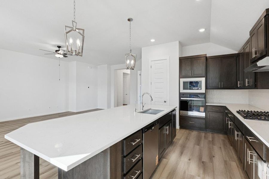 Kitchen with dark brown cabinets, decorative light fixtures, light wood finished floors, decorative backsplash, and stainless steel appliances Kitchen with dark brown cabinets, decorative light fixtures, light wood finished floors, decorative backsplash, and stainless steel appliances