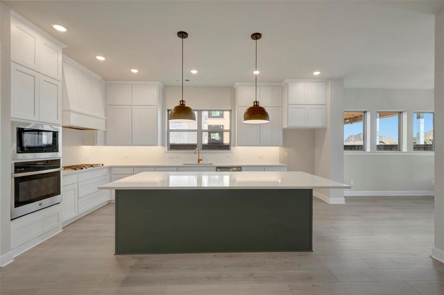 Dual tone kitchen with a center island, stainless steel appliances, hanging light fixtures, light wood-type flooring, and dual tone cabinets