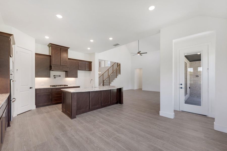 Open kitchen with dark wood cabinets, large island with light countertop, and gray hardwood floors