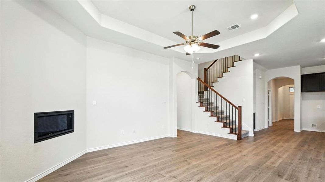 Unfurnished living room featuring arched walkways, light wood-type flooring, recessed lighting, ceiling fan, and a raised ceiling