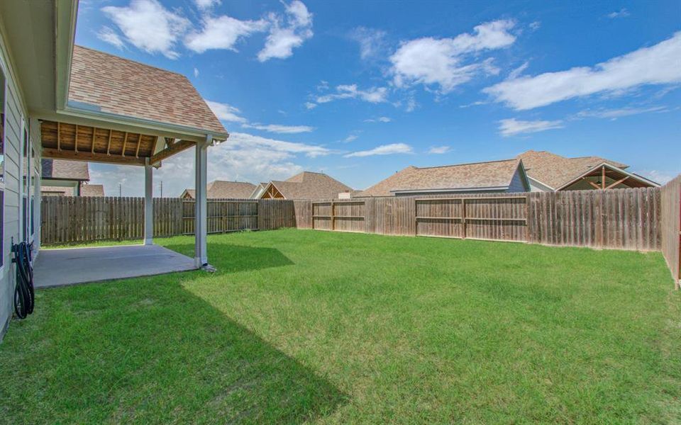 This is a spacious backyard with a well-maintained lawn and a privacy fence, featuring a covered patio area that's perfect for outdoor relaxation or entertainment. The surrounding area includes similar residential properties, suggesting a cohesive neighborhood setting.