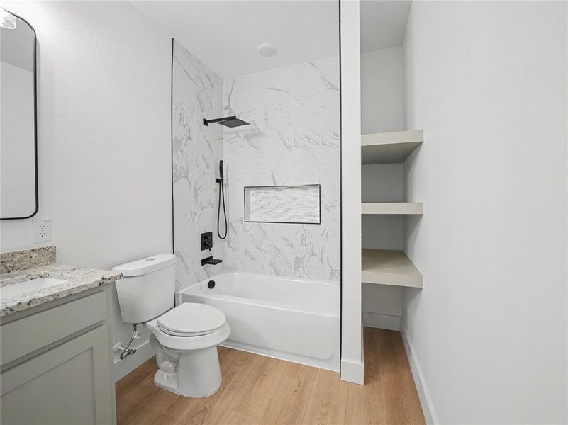 Contemporary bathroom featuring a white tub with marble-patterned tile surround, matte black shower fixtures, a built-in shower niche, and light wood-finish flooring Contemporary bathroom featuring a white tub with marble-patterned tile surround, matte black shower fixtures, a built-in shower niche, and light wood-finish flooring