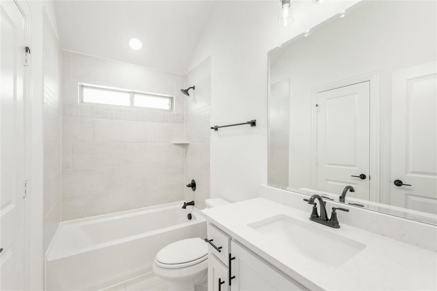 Bathroom with white vanity, tiled tub-shower combo, and black fixtures on vaulted ceiling