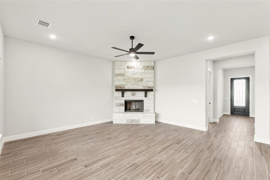 Open living room with stone fireplace, ceiling fan, and wood-look tile floors Open living room with stone fireplace, ceiling fan, and wood-look tile floors