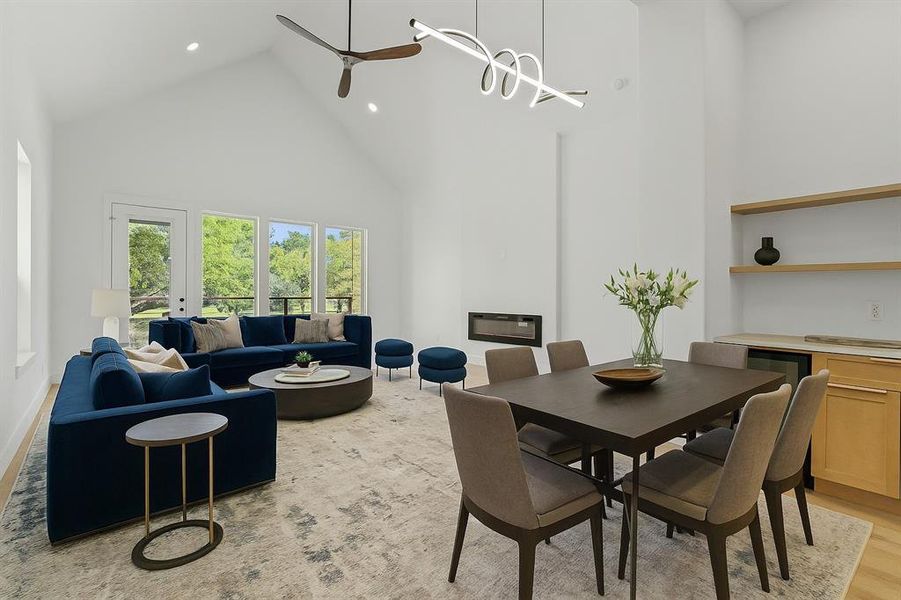 Digitally staged space featuring high vaulted ceiling, light wood finished floors, ceiling fan, recessed lighting, and a glass covered fireplace