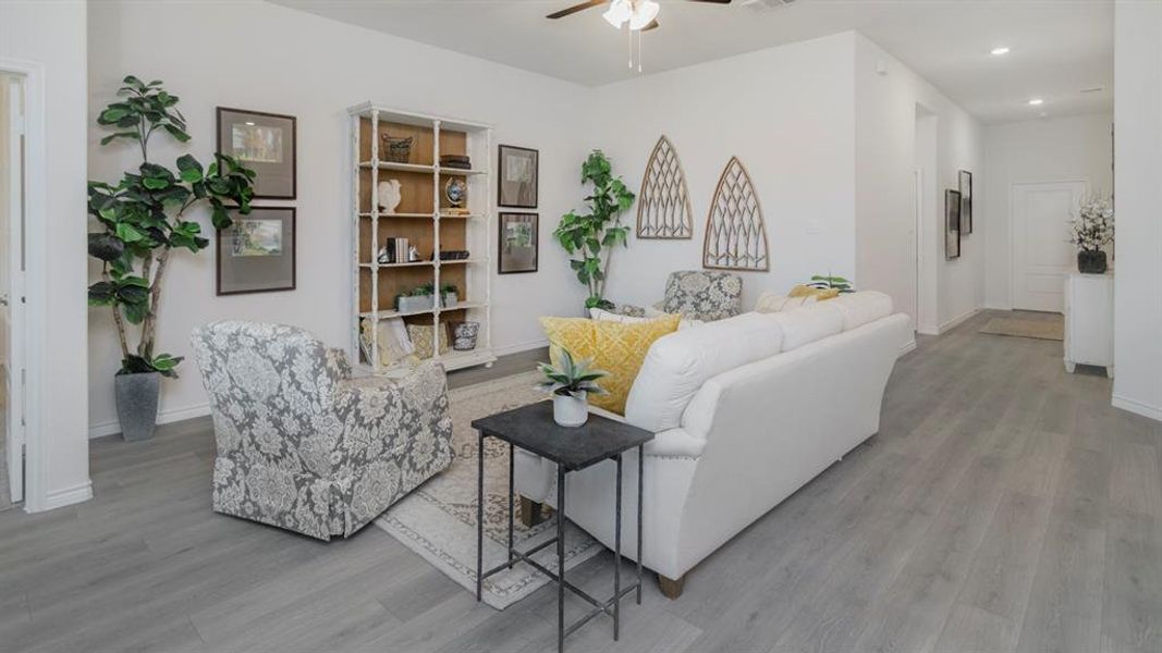 Open-concept living area featuring light-toned wood-finish flooring, a ceiling fan, white walls, and a built-in shelving unit