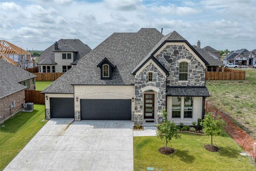 French provincial home with stone siding, brick siding, driveway, a residential view, and a shingled roof