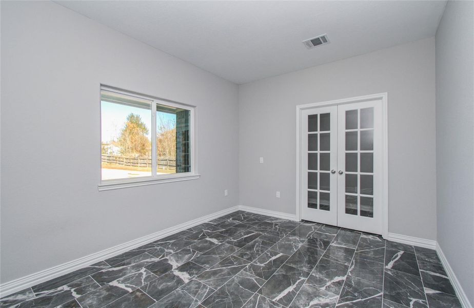 This bright room features marble-patterned tile flooring, a large window for natural light, and elegant French doors. Perfect for a home office or study.
