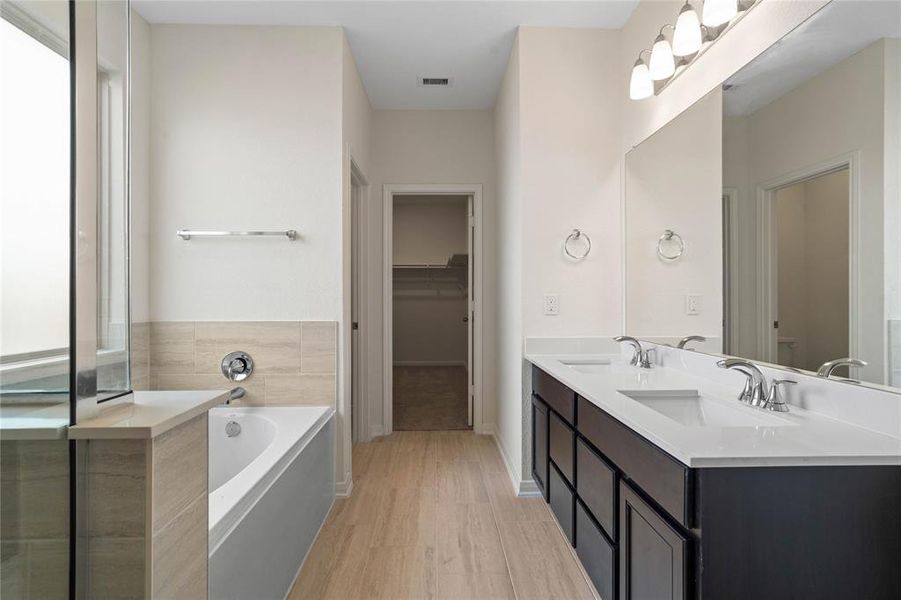 This primary bathroom is definitely move-in ready! Featuring an oversized tub and shower combo with tile surround, stained cabinets with light countertops, dual vanities, high ceilings, neutral paint, sleek and modern finishes.