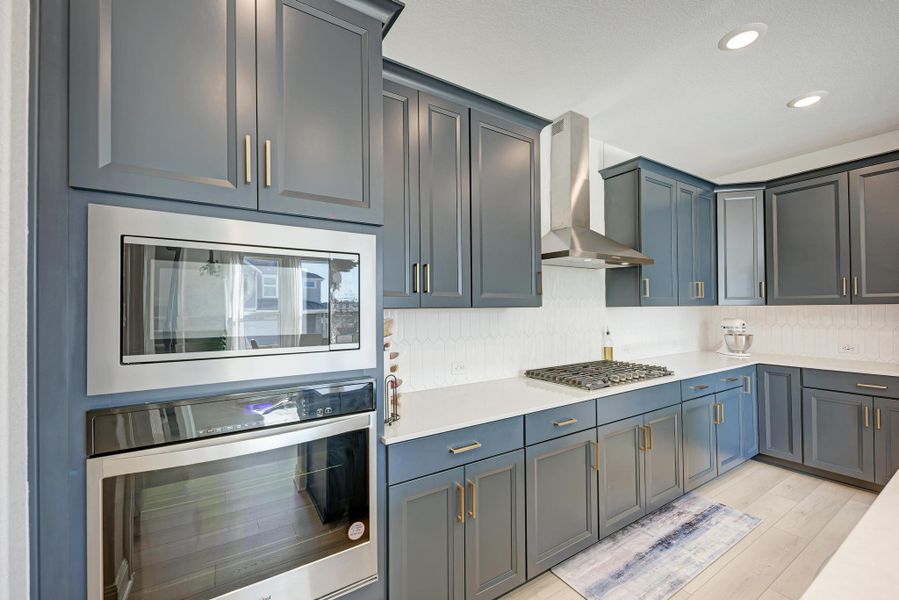 Kitchen with appliances with stainless steel finishes, wall chimney exhaust hood, tasteful backsplash, light wood-type flooring, and recessed lighting