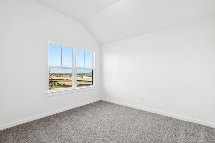 Carpeted empty room with vaulted ceiling and baseboards Carpeted empty room with vaulted ceiling and baseboards