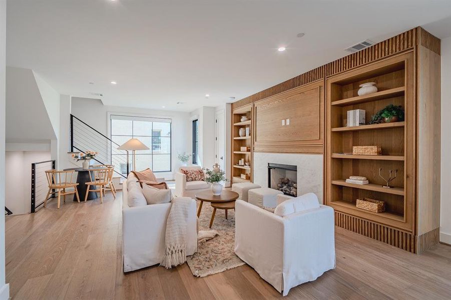 Living room featuring light wood finished floors, a fireplace, recessed lighting, and built in shelves