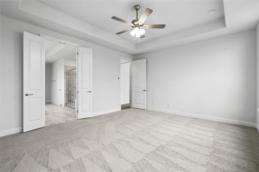 Unfurnished bedroom featuring a ceiling fan, a raised ceiling, carpet floors, and baseboards