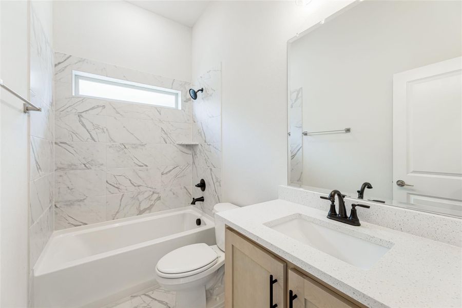Bathroom with marble-look tile tub surround, white quartz vanity, and wood cabinet with black fixtures