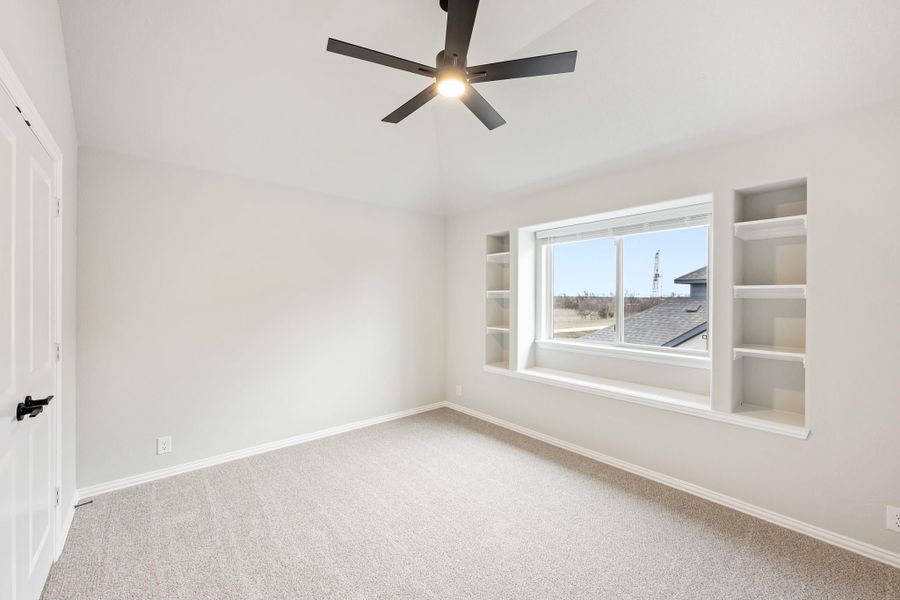 Empty bedroom with carpet, ceiling fan, and built-in shelves flanking a large window Empty bedroom with carpet, ceiling fan, and built-in shelves flanking a large window