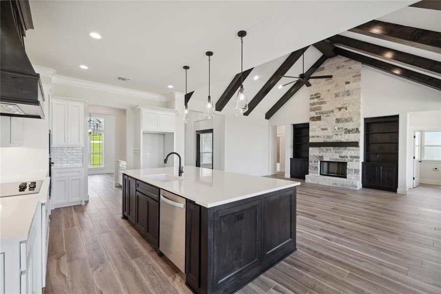 Kitchen with stainless steel dishwasher, sink, lofted ceiling with beams, a center island with sink, and a stone fireplace