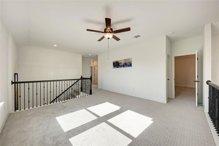 Spacious carpeted bonus room featuring a ceiling fan with light, recessed lighting, and a black wrought iron railing overlooking the staircase