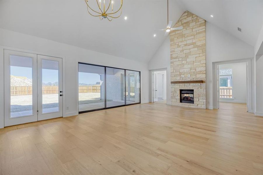 Unfurnished living room featuring a high ceiling, light wood finished floors, healthy amount of natural light, a fireplace, and a ceiling fan