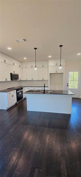 Kitchen with dark countertops, decorative light fixtures, white cabinets, stainless steel appliances, and dark wood-type flooring Kitchen with dark countertops, decorative light fixtures, white cabinets, stainless steel appliances, and dark wood-type flooring