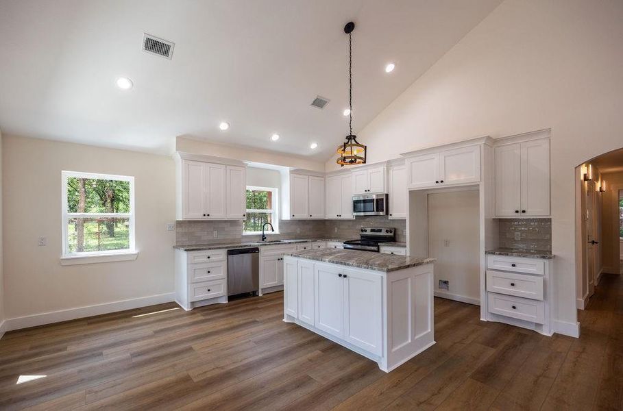 Kitchen featuring white cabinets, arched walkways, decorative backsplash, pendant lighting, and high vaulted ceiling
