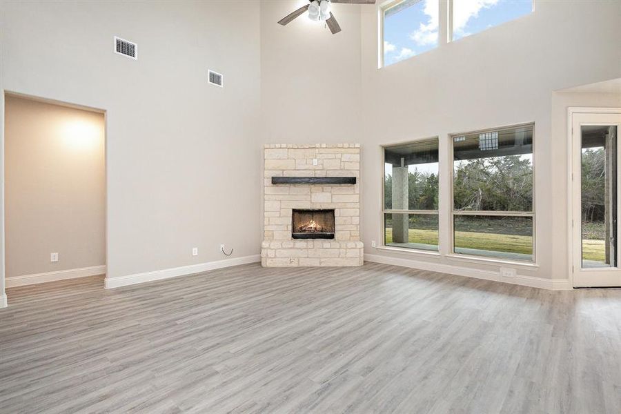 Unfurnished living room featuring a stone fireplace, ceiling fan, a healthy amount of sunlight, and a high ceiling