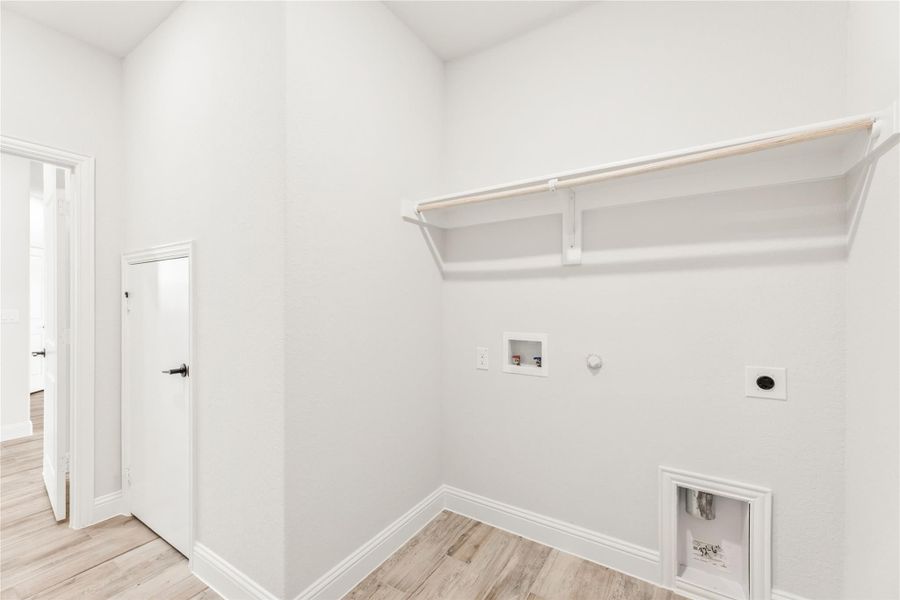 Laundry room with wall-mounted shelf, washer hookups, dryer outlet, and light wood floors Laundry room with wall-mounted shelf, washer hookups, dryer outlet, and light wood floors