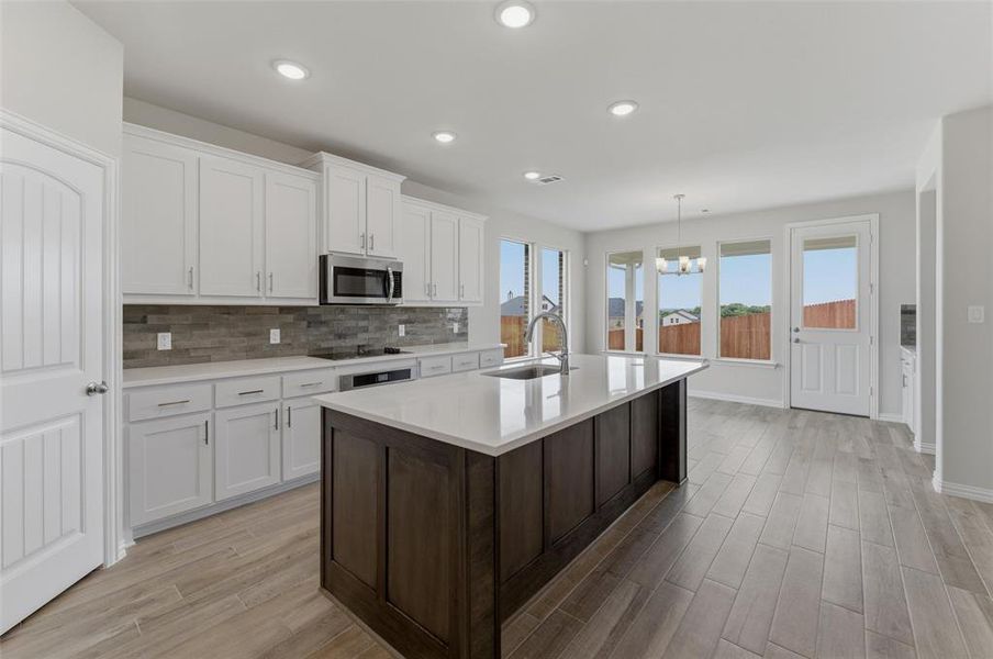 Open-concept kitchen featuring an oversized island with a stainless steel sink, white shaker cabinetry, and wood-finish flooring